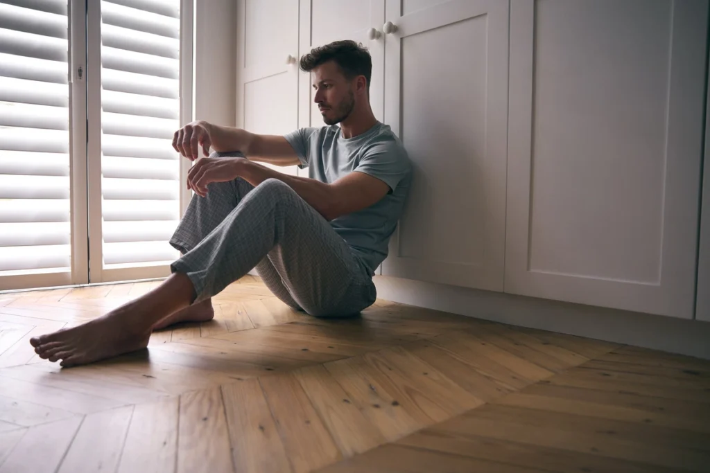 Addiction and Mental Health - man sitting on bedroom floor depressed