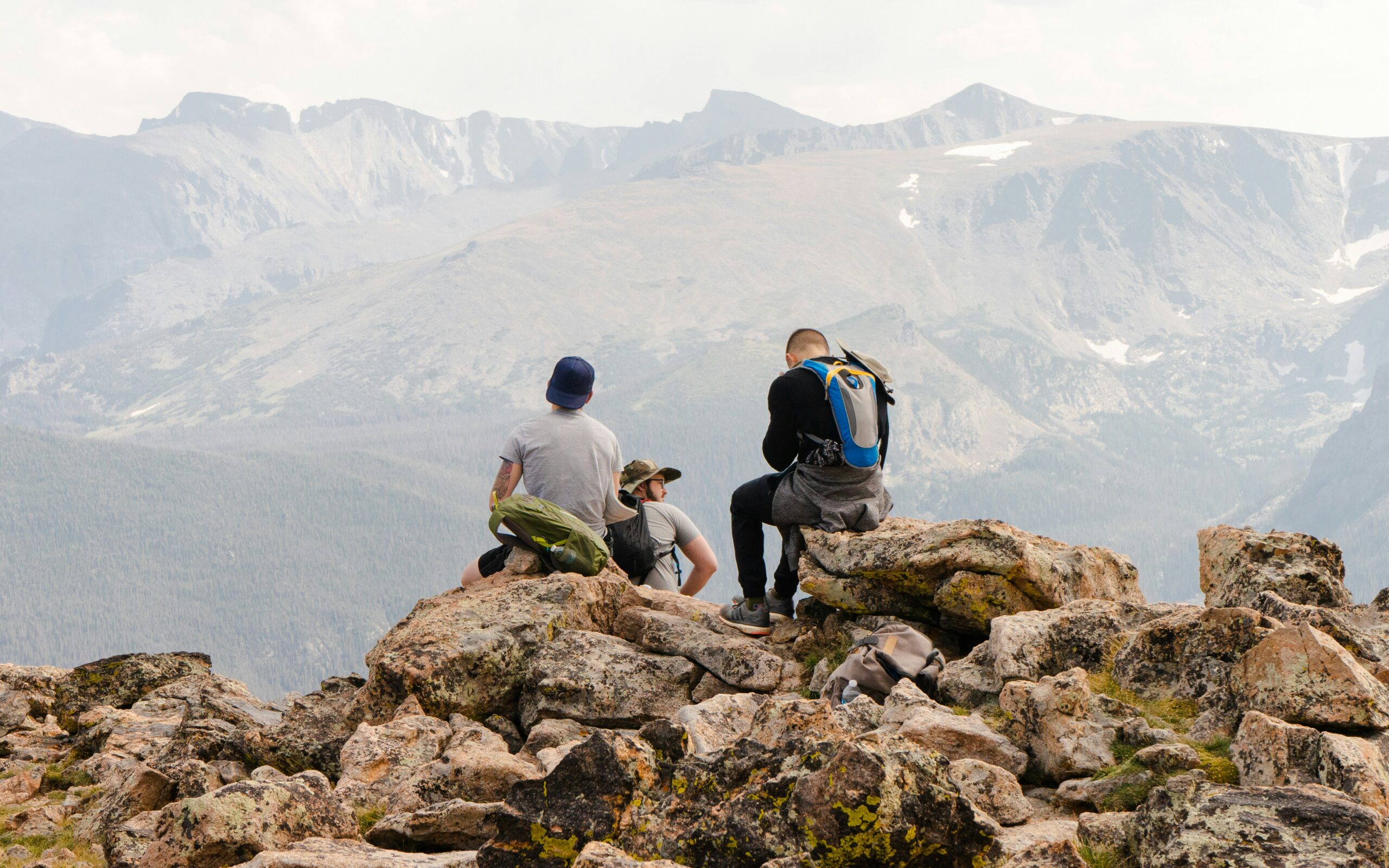 Three men sitting together on a rocky outcrop high in the Colorado Rockies, looking out across the mountains.